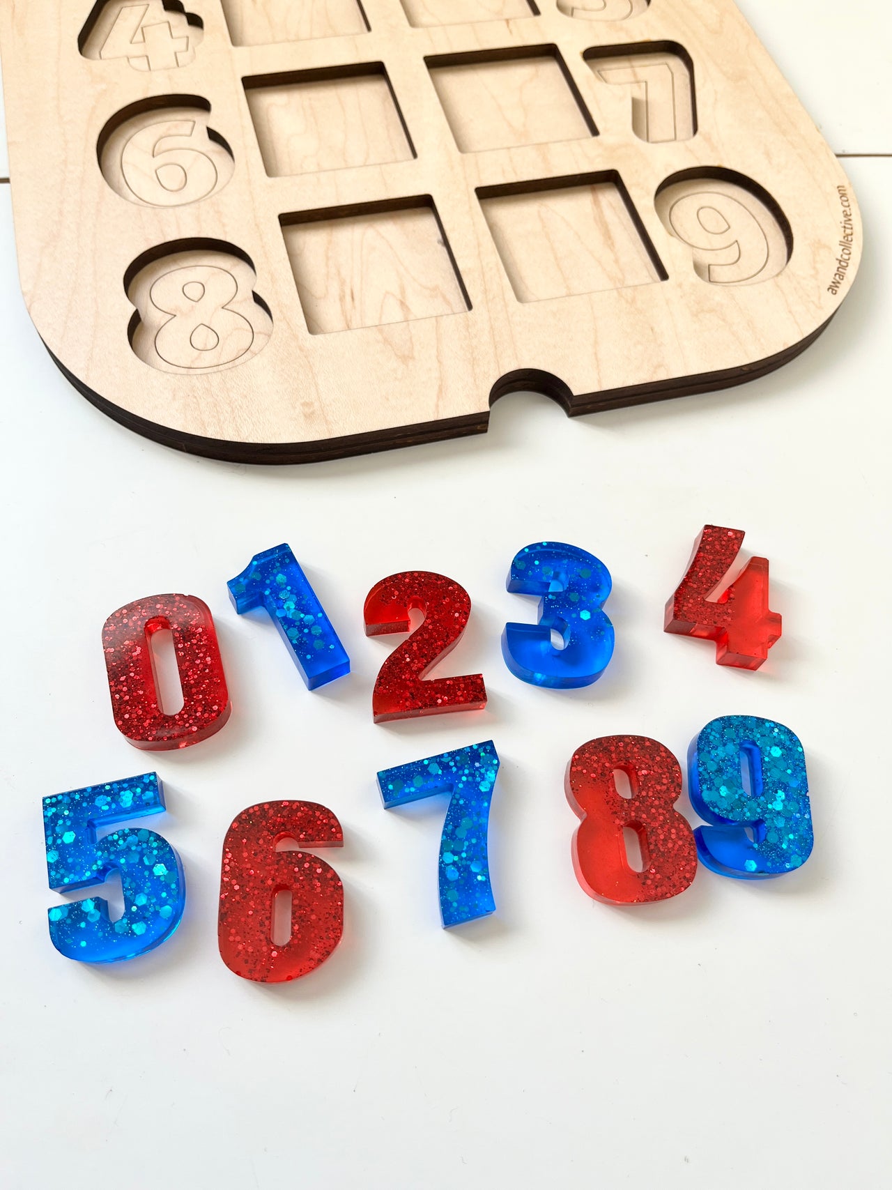 Glitter-filled red and blue resin numbers zero through nine displayed near a wooden number puzzle board