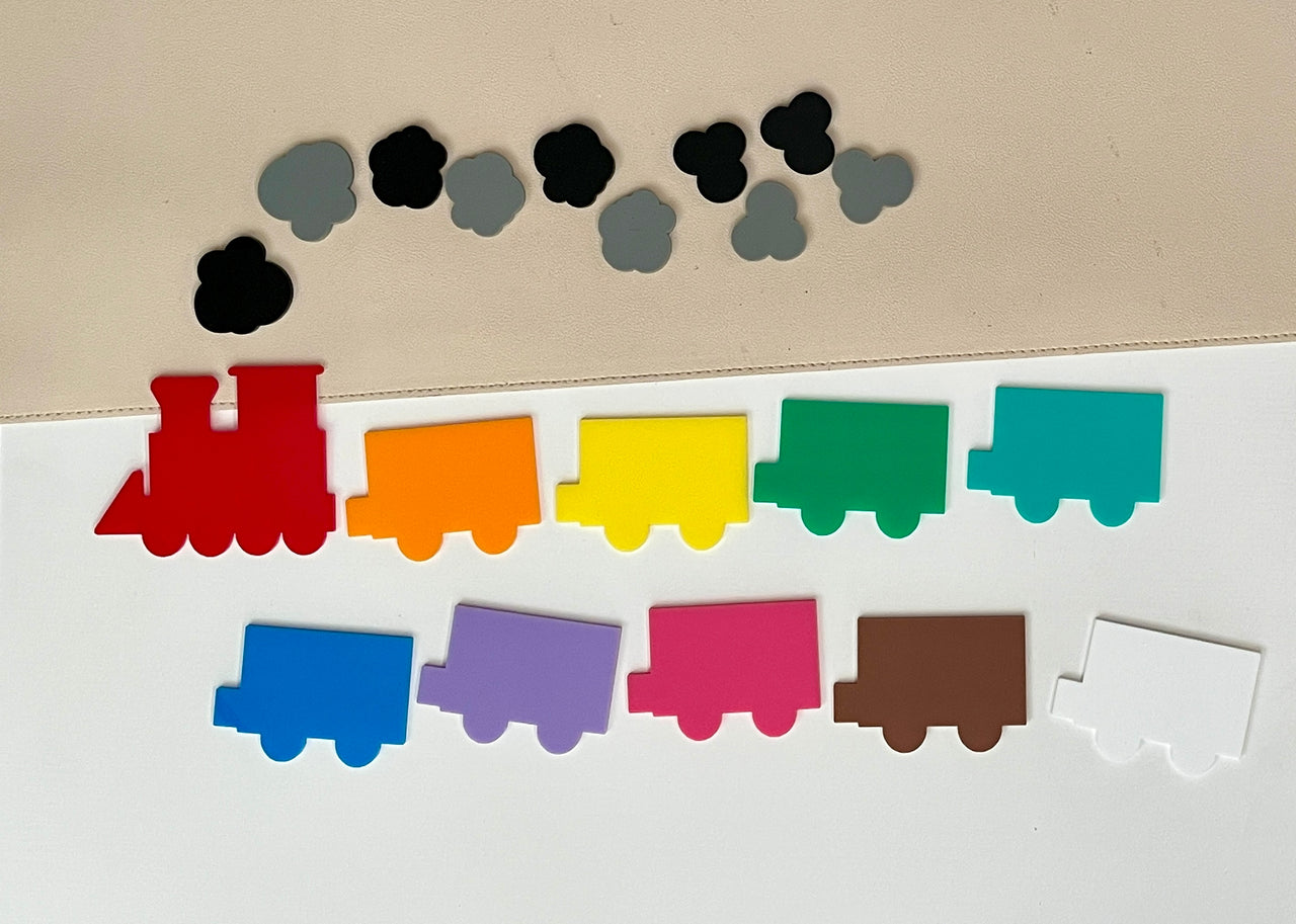 Colorful wooden train pieces and black and gray cloud-shaped pieces arranged on a white and beige surface