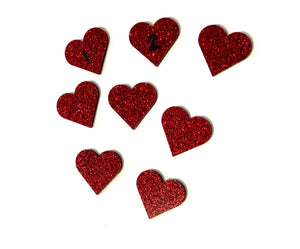 Eight small red glittery heart-shaped embellishments scattered on a white background