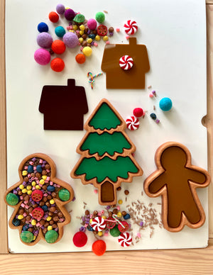 Wooden gingerbread man, tree, and house trays with colorful craft pom-poms, beads, and candy-shaped decorations scattered nearby