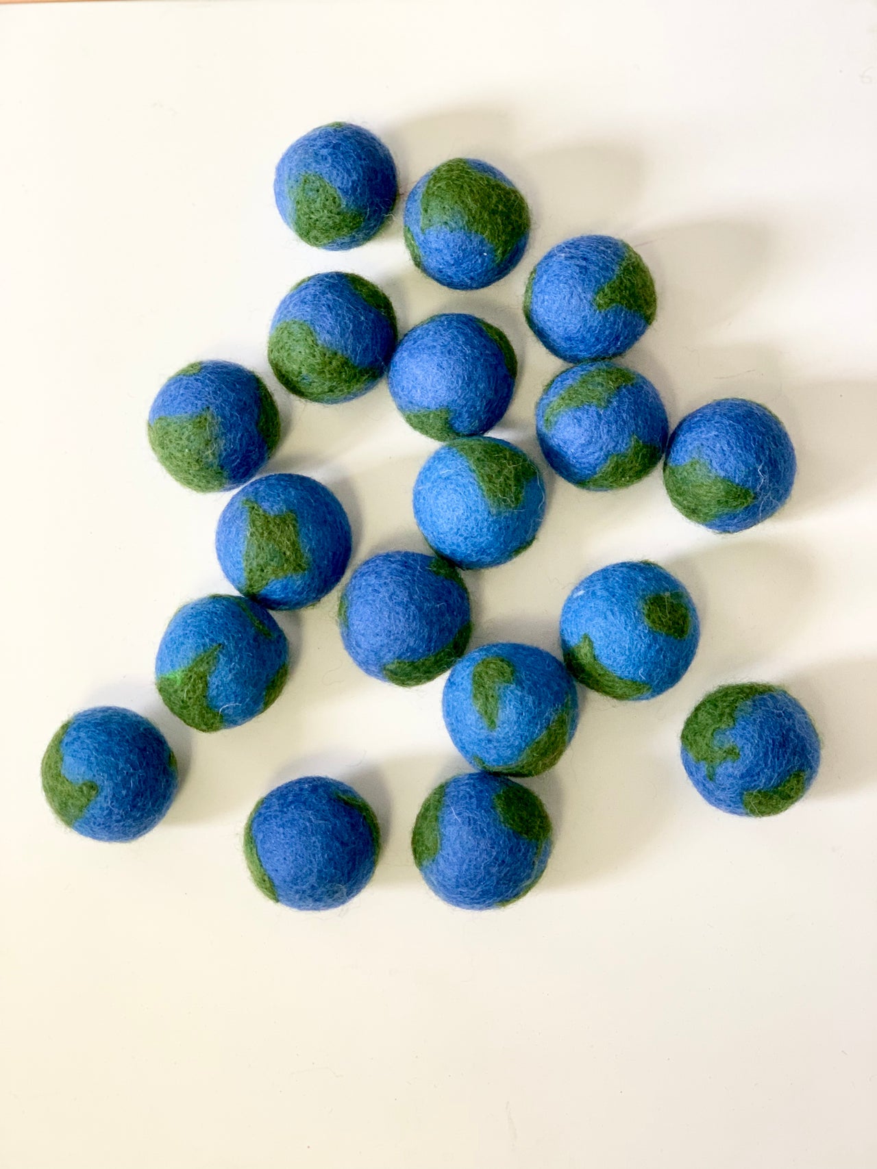 Group of small handmade felt globes in blue and green wool arranged on white background