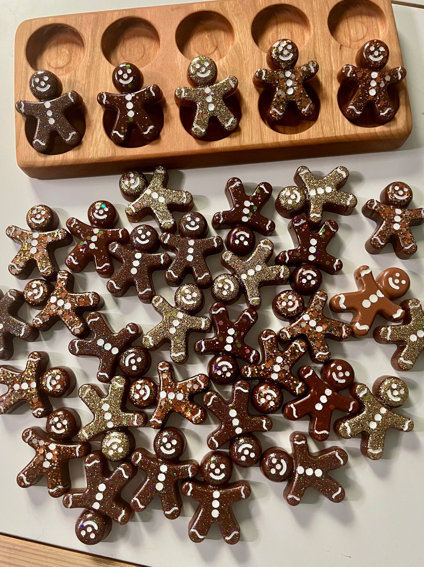 Chocolate resin gingerbread men on a white surface with a wooden ten frame in the background.