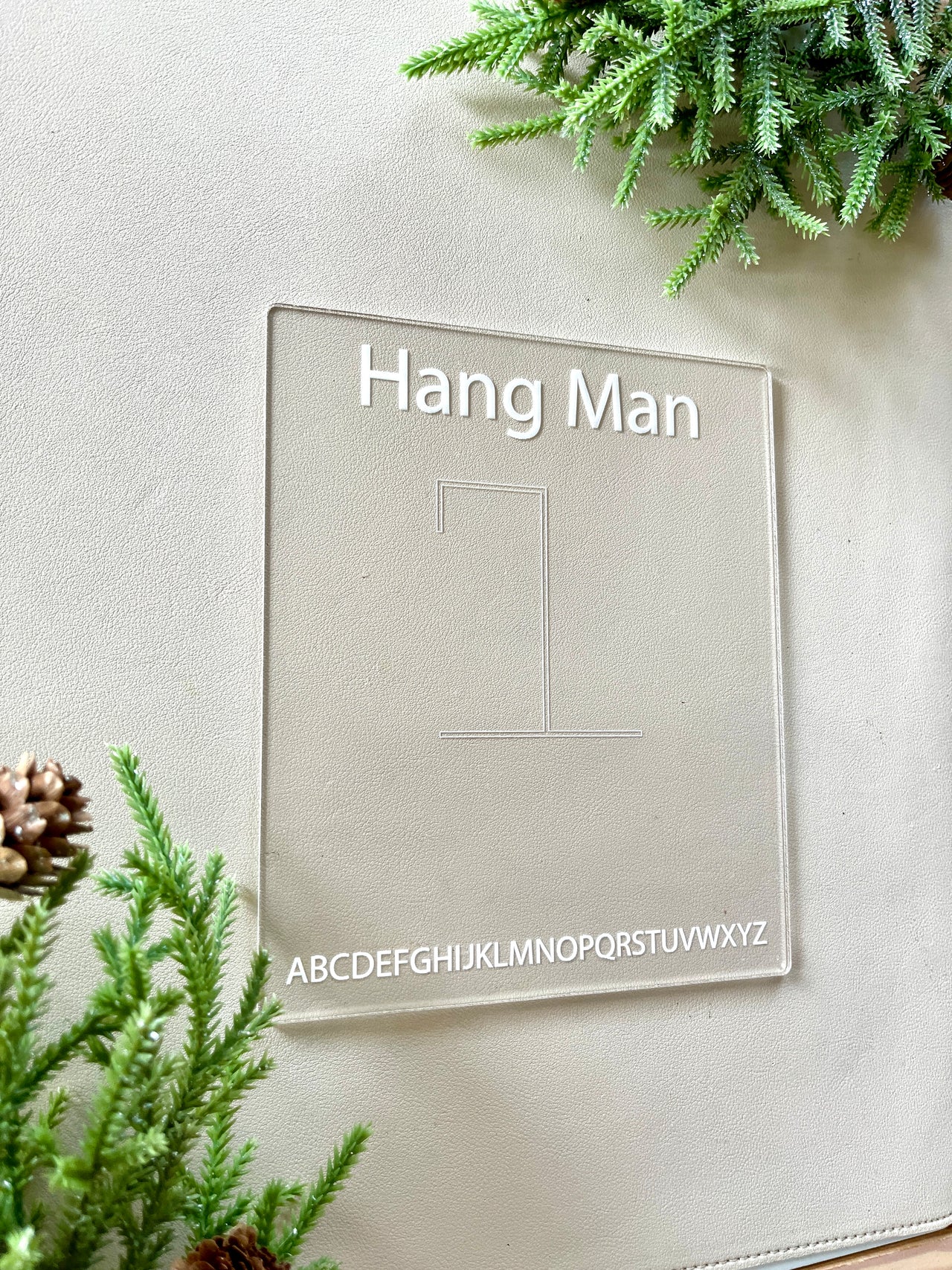 Clear acrylic Hangman game board with engraved letters and gallows outline surrounded by pine branches and cones