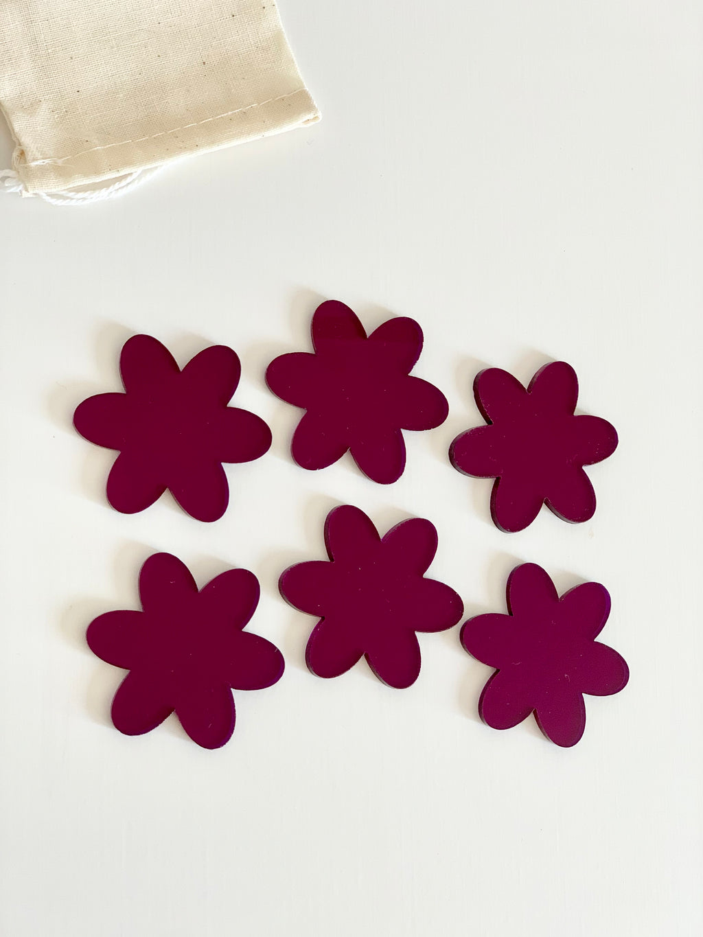 Set of six dark magenta flower-shaped dry erasable pieces arranged on white surface with fabric pouch corner visible