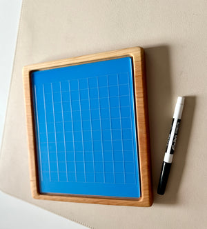 Wooden-framed blue magnetic board with grid lines next to a black and white dry erase marker on beige surface