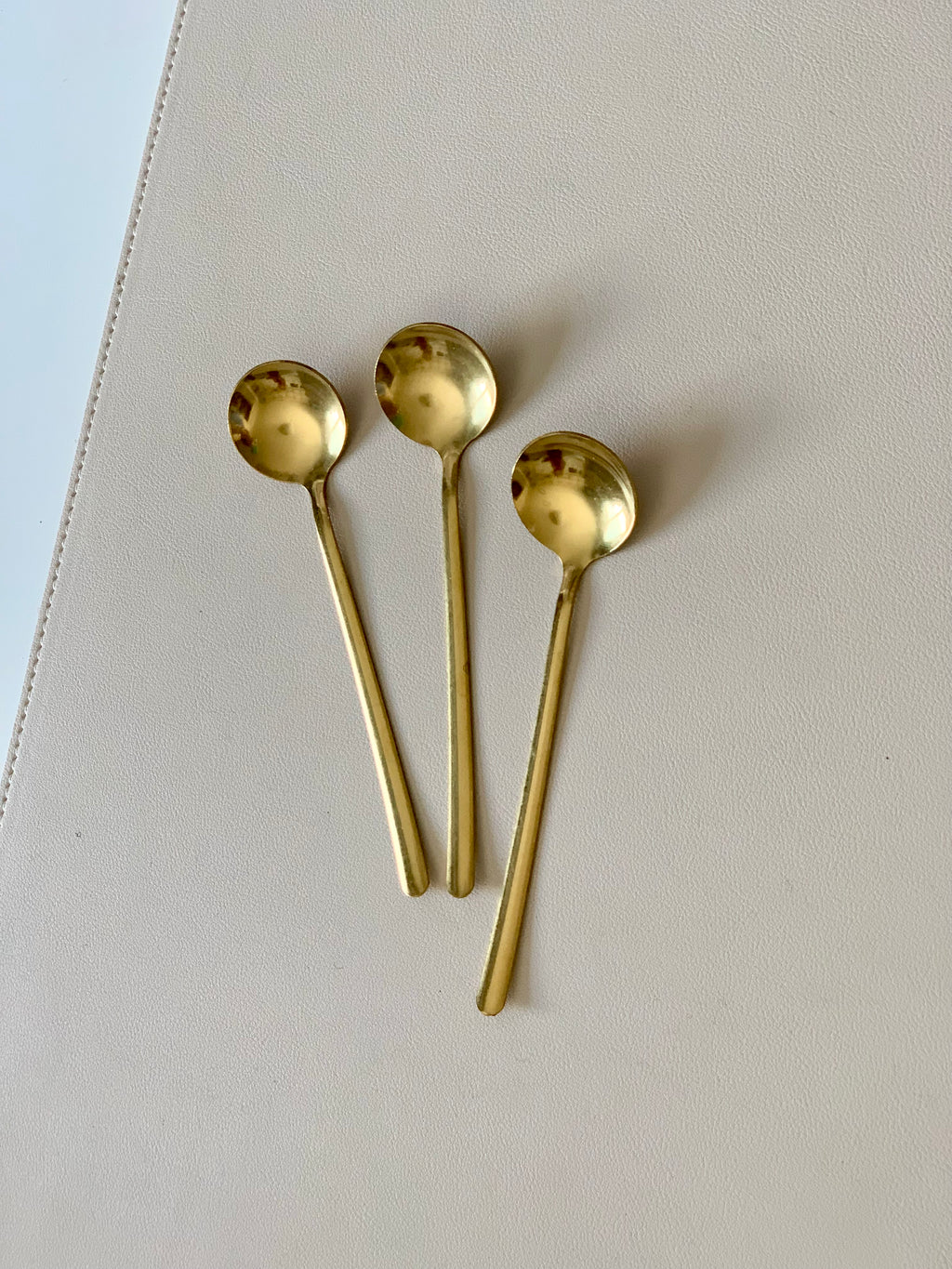 Three small gold-toned spoons with rounded bowls arranged on a light beige textured surface