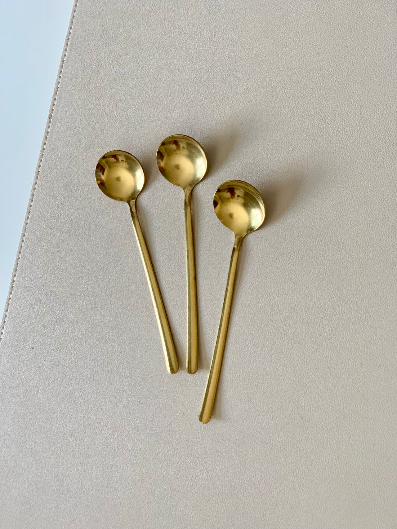 Three small gold-toned spoons with rounded bowls arranged on a light beige textured surface