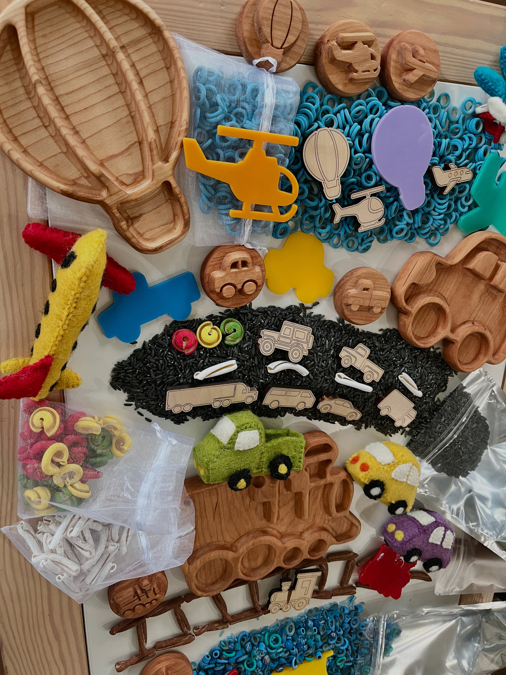 Assorted wooden vehicle shapes, colorful felt cars, and craft supplies arranged on a wooden table surface.