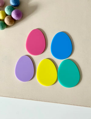 Five brightly colored plastic egg-shaped pieces arranged on a beige surface near multicolored felt balls