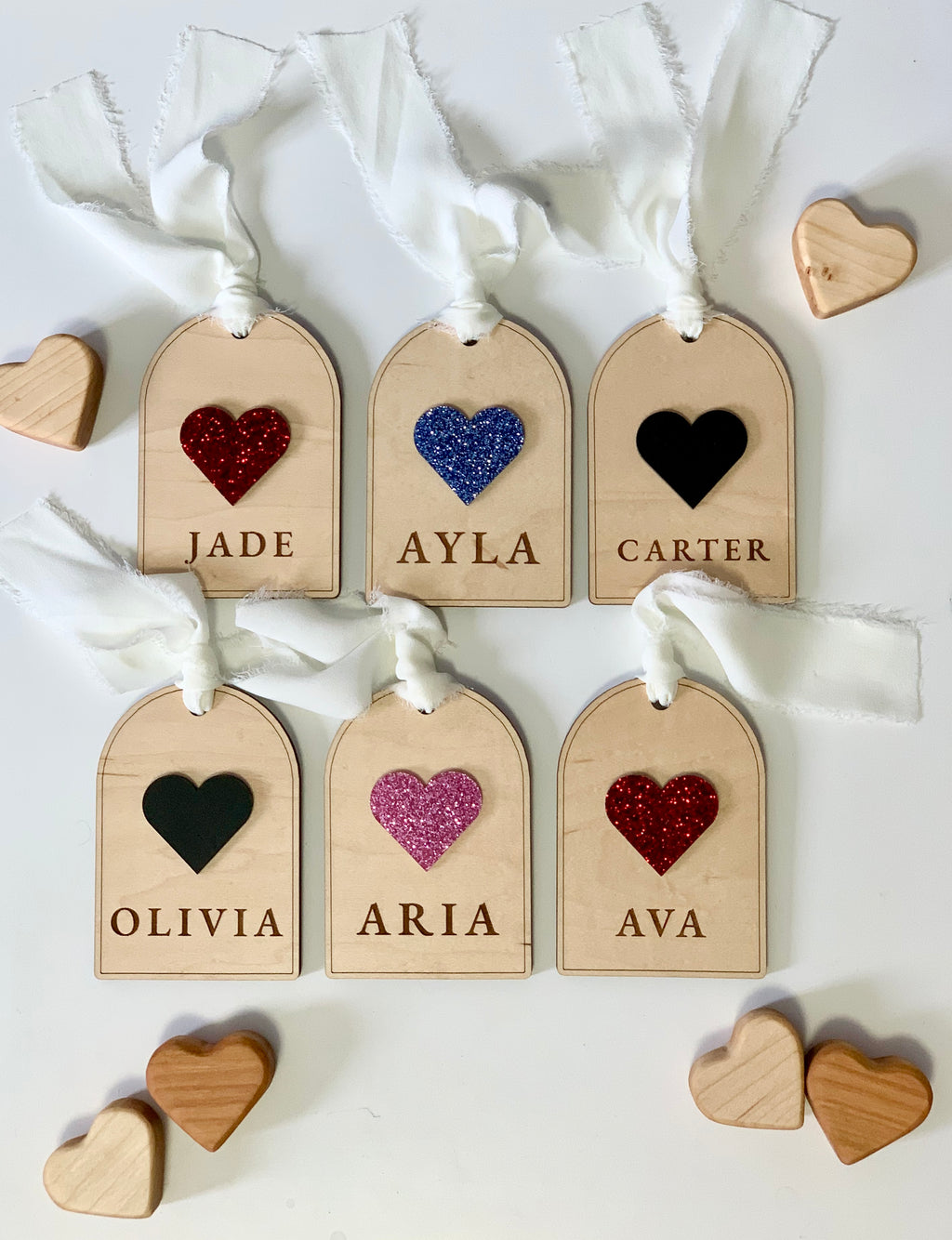 Set of six wooden gift tags with glittery and solid heart shapes and engraved names tied with white fabric ribbons