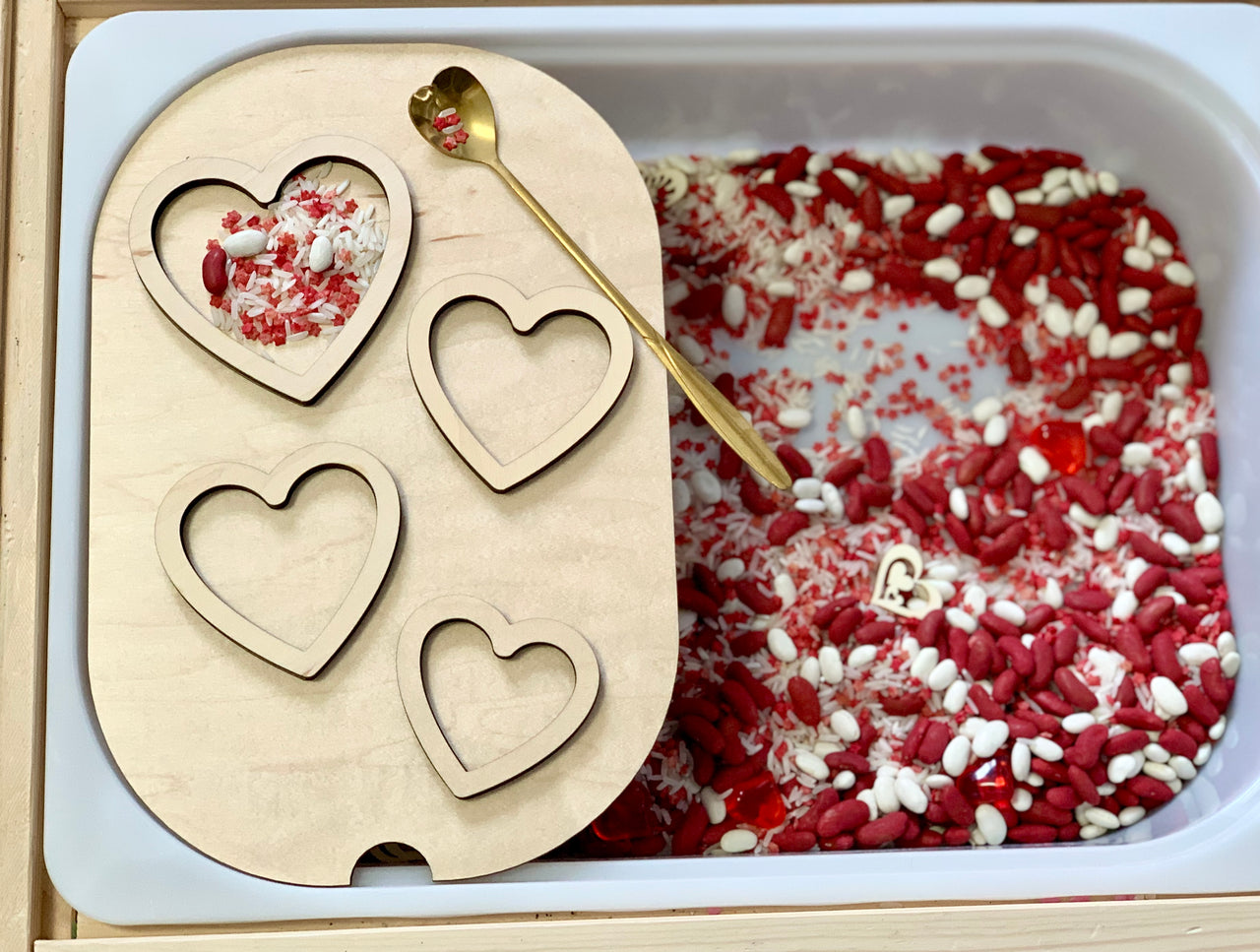 Wooden tray with four heart-shaped cutouts over a bin filled with red and white rice and a gold spoon with a heart-shaped handle