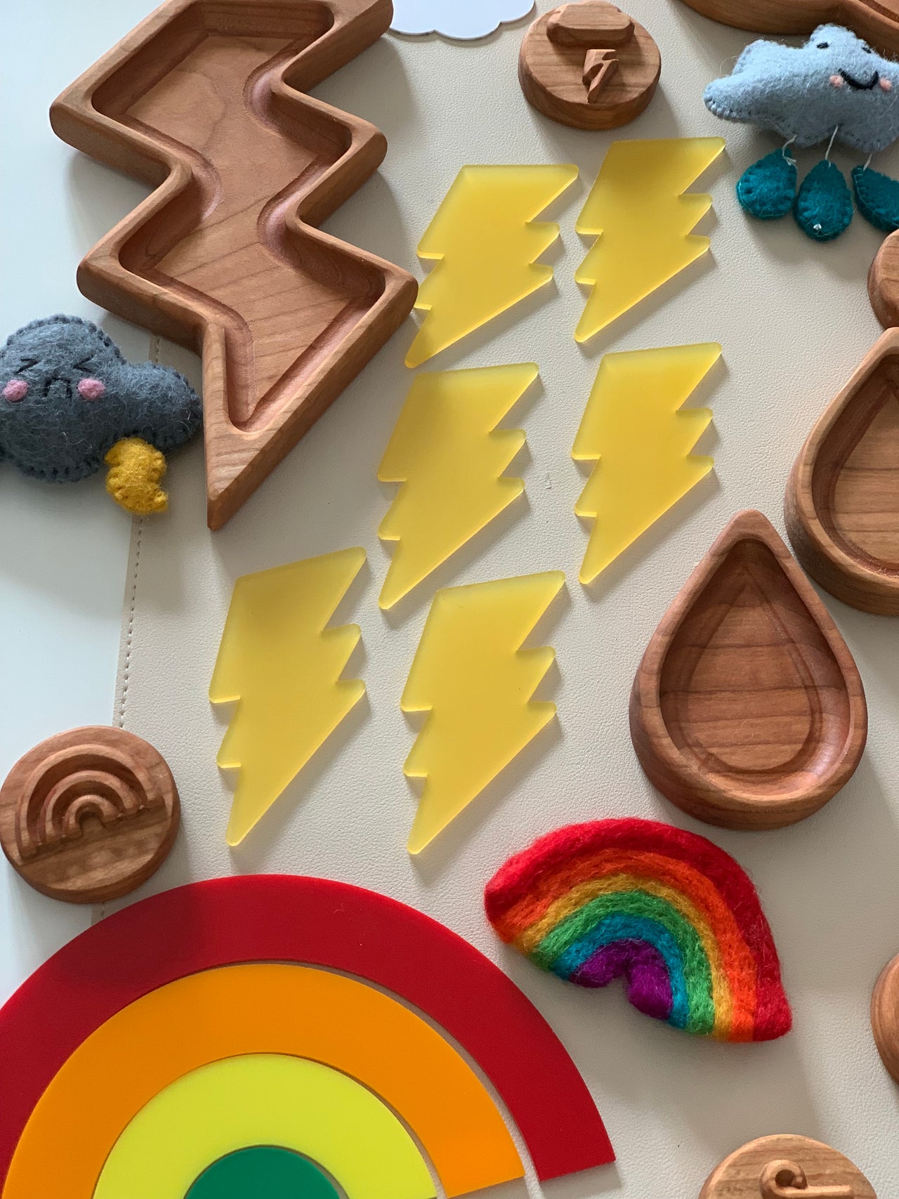 Seven translucent yellow lightning bolt shapes arranged beside wooden trays and colorful felt weather figures on a white surface