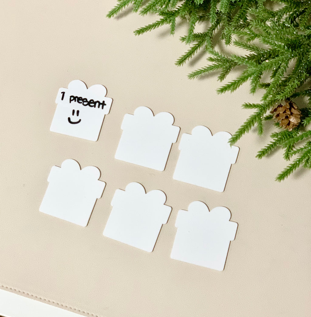 Set of six white little dry erasable cards shaped like presents on beige surface with pine branch decoration