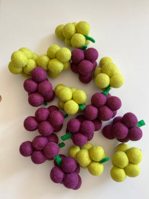 Clusters of small felted balls in yellow and purple arranged to resemble bunches of grapes on a white surface