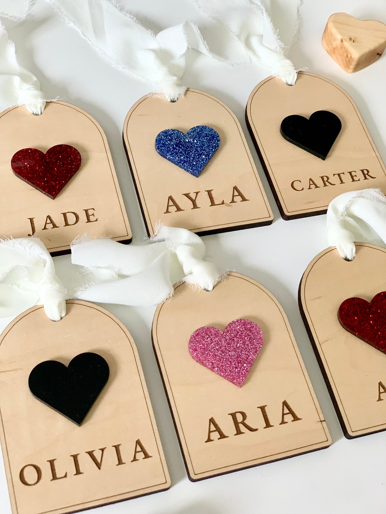 Set of wooden gift tags with glittery and solid heart embellishments and names engraved, tied with white fabric ribbons