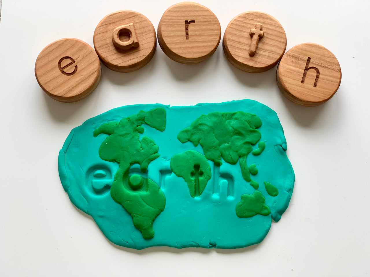 Wooden letter tokens spelling "earth" above blue and green playdough shaped like a world map with the word earth embossed