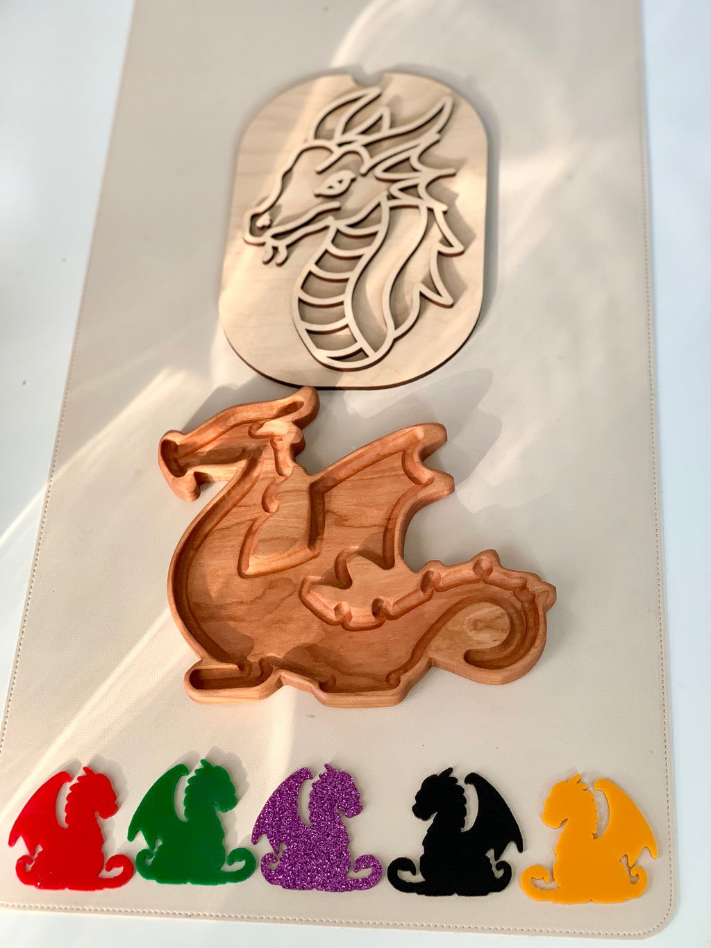 Wooden dragon tray with dragon-shaped colorful plastic pieces in red, green, purple glitter, black, and yellow below it on white surface