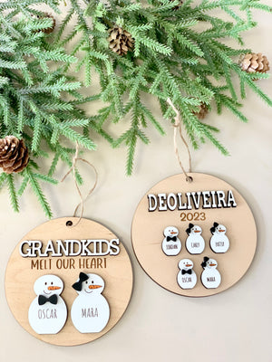 Personalized wooden Christmas ornaments with snow person figures and names, hanging on a pine branch background