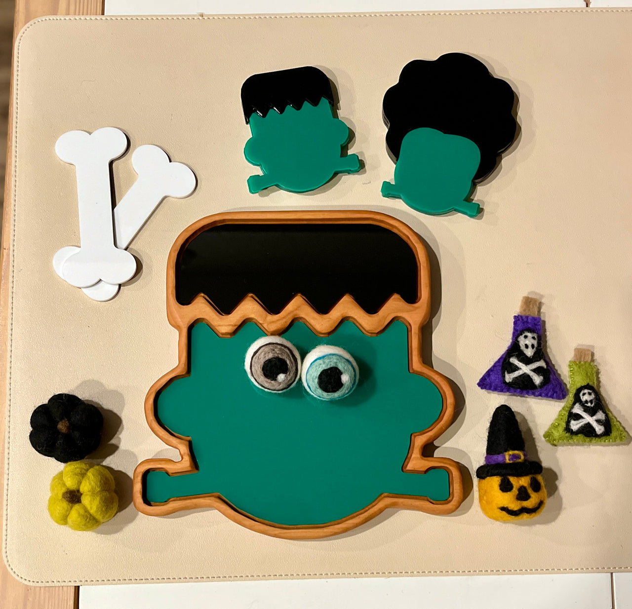 Wooden puzzle pieces shaping a green Frankenstein head with separate hair pieces and felt Halloween decorations surrounding it