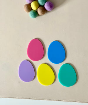 Five colorful egg-shaped pieces arranged in a semicircle on a light surface with felt balls above them
