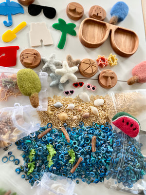 Assorted wooden and felt shapes, colorful sensory beads, shells, dried pasta, and playful miniature accessories on a white surface