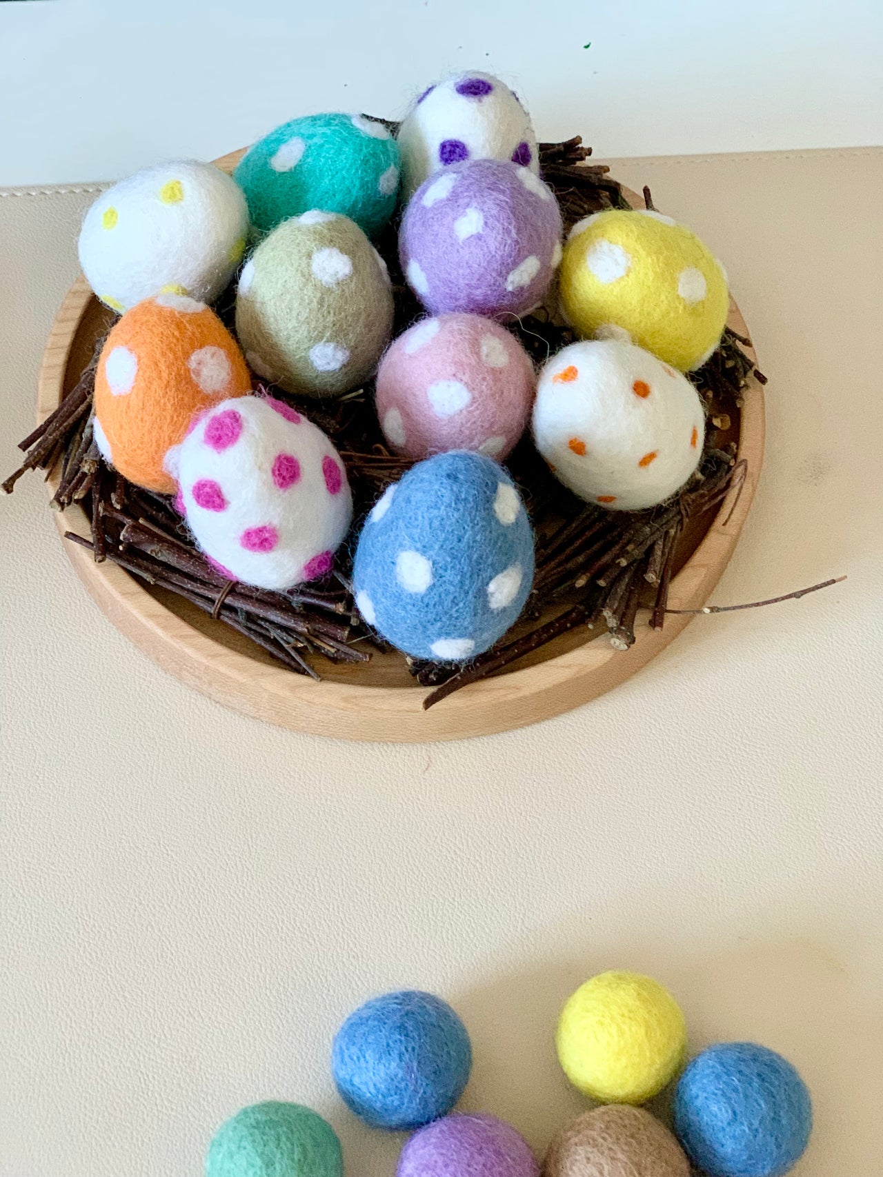 Nest of twigs holding colorful felt eggs with white, pink, and orange polka dots on a wooden base