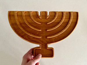 Handheld wooden serving tray carved in the shape of a menorah with seven curved branches on a neutral background