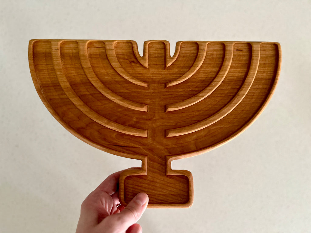 Handheld wooden serving tray carved in the shape of a menorah with seven curved branches on a neutral background