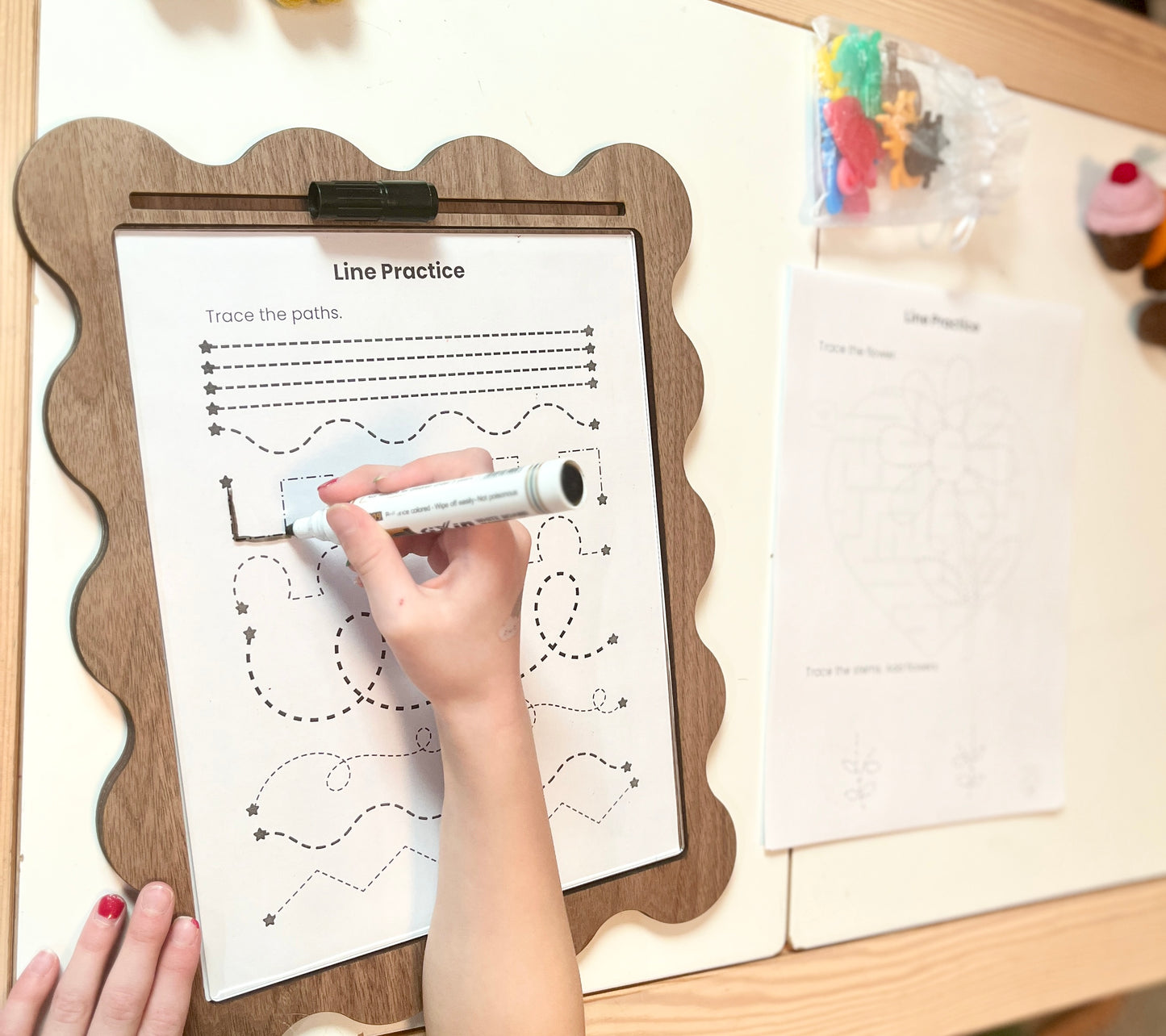Child tracing lines on a worksheet with a wooden tray with dry erase insert.