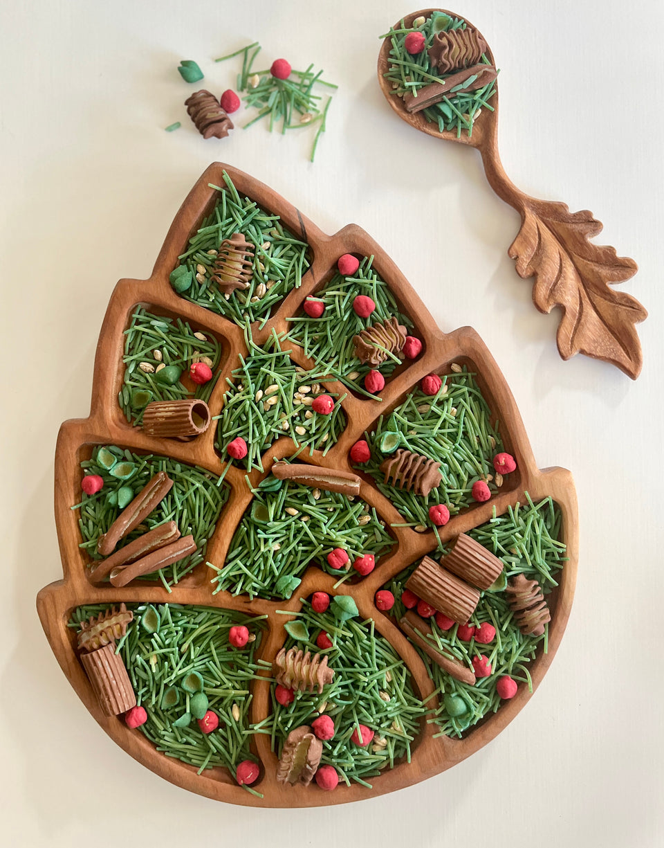 Wooden leaf-shaped serving tray with green herbs, red berries, cinnamon sticks, and a matching wooden serving spoon with leaf handle