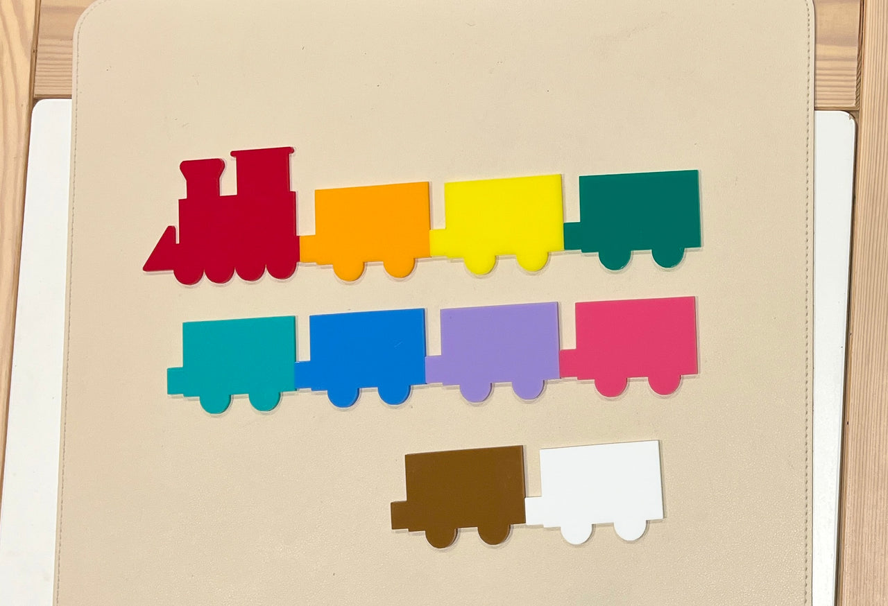 Colorful flat wooden train shapes in red, orange, yellow, green, teal, blue, purple, pink, brown, and white on a light background