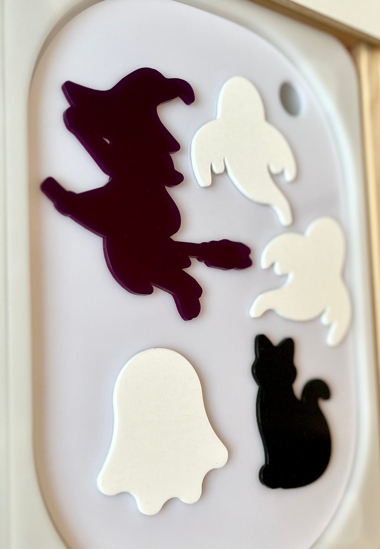 Halloween-themed wooden shapes of a witch on a broom, three ghosts, and a black cat on a white tray