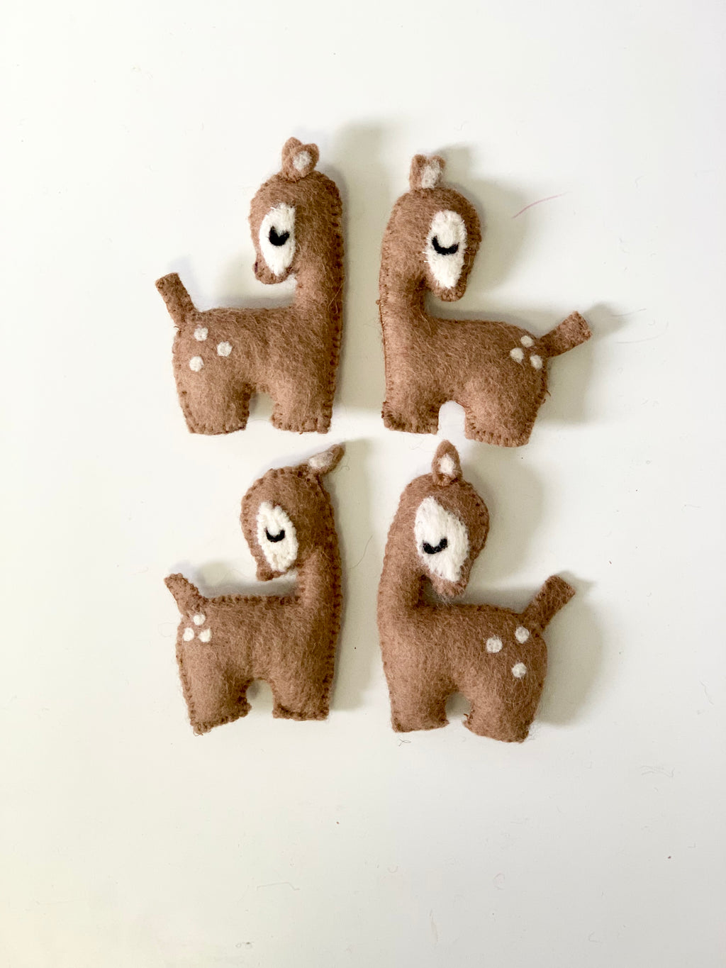 Set of four handmade felt deer toys in brown and white with closed eyes on white background