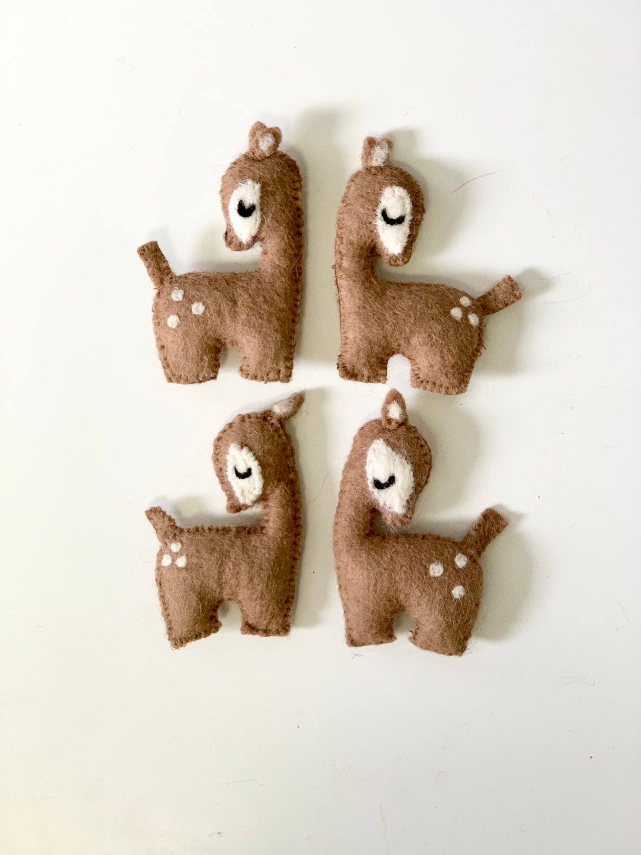 Set of four handmade felt deer toys in brown and white with closed eyes on white background