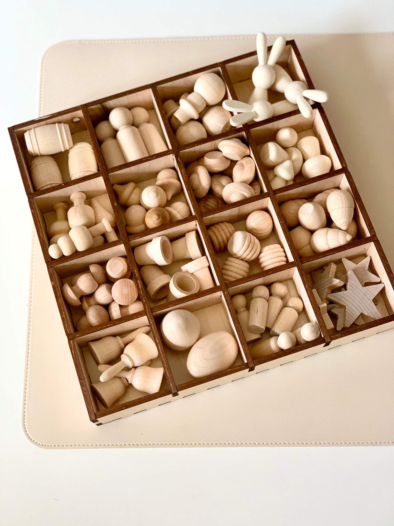 Compartmentalized wooden tray containing various unfinished wooden shapes including animals, spools, stars, and abstract figures