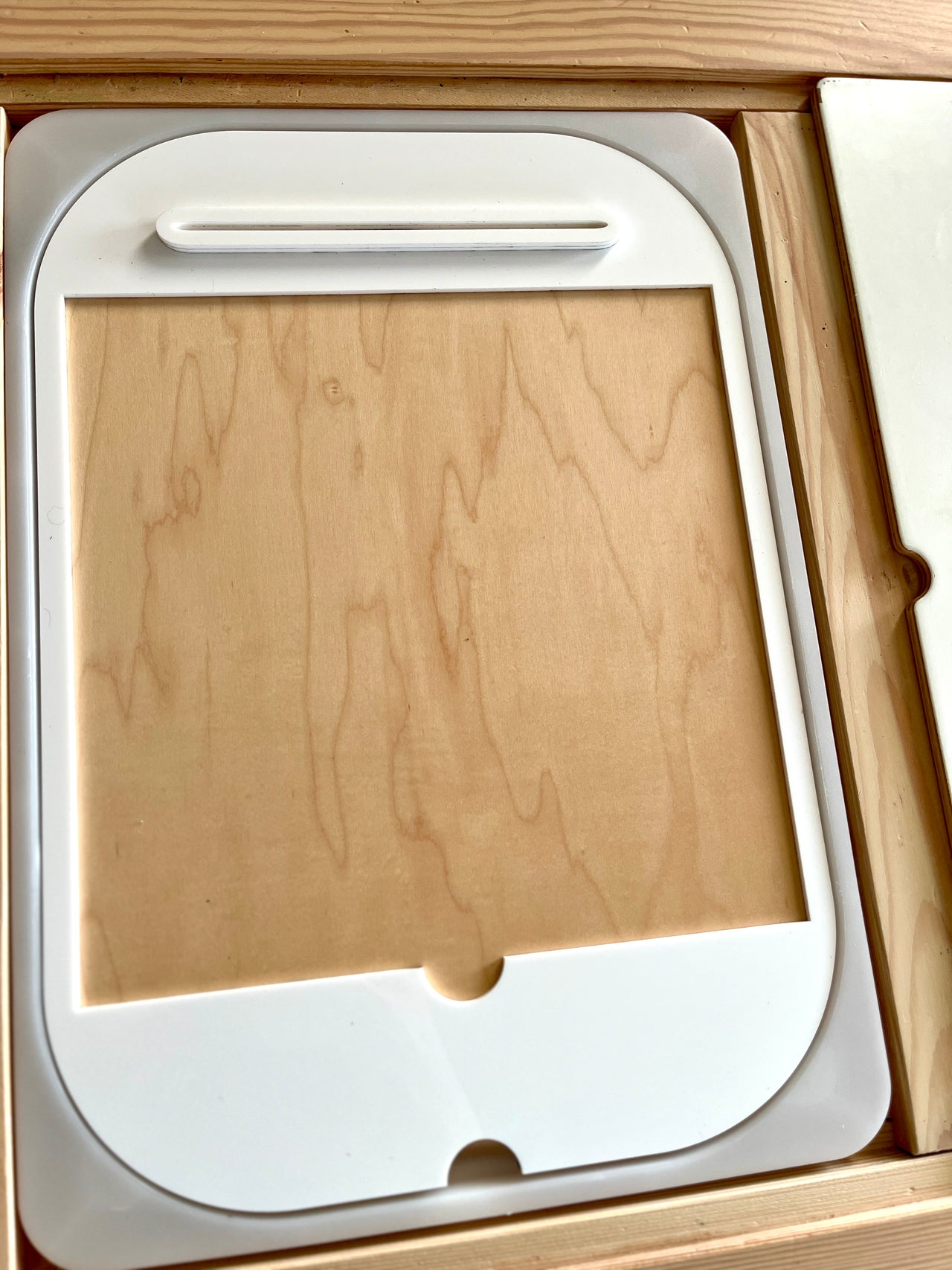 White plastic frame with rounded edges resting inside a wooden box on a wooden surface