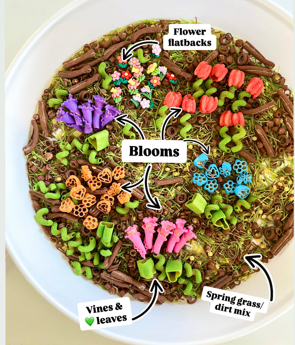 Bowl containing colorful flower-shaped flatbacks, vibrant blooms, green vines, leaves, and spring grass with dirt mix