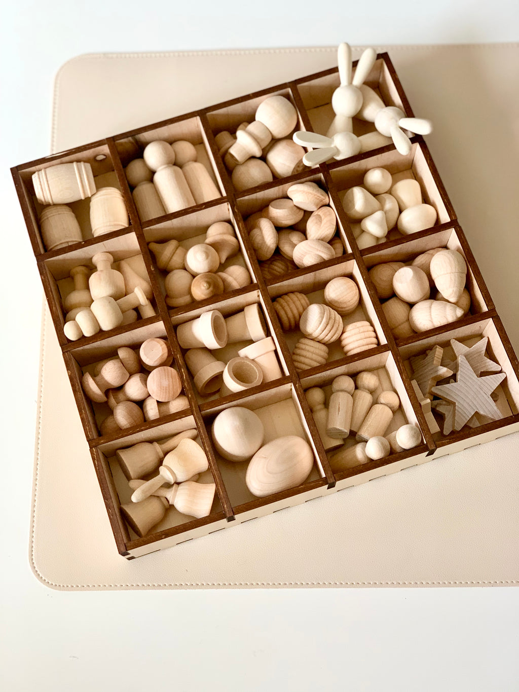 Wooden tray with multiple compartments holding assorted smooth unfinished wooden shapes including figures and geometric forms