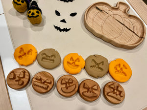 Wooden and clay discs engraved with various Halloween pumpkin faces arranged near a wooden pumpkin-shaped dish and felt pumpkin decorations
