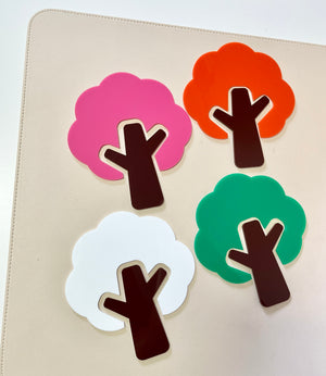 Four flat tree shapes in pink, orange, white, and green with dark brown trunks on a beige surface