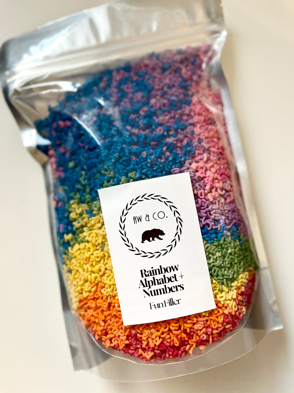 Clear pouch filled with multicolored small alphabet and number shapes arranged in rainbow sections
