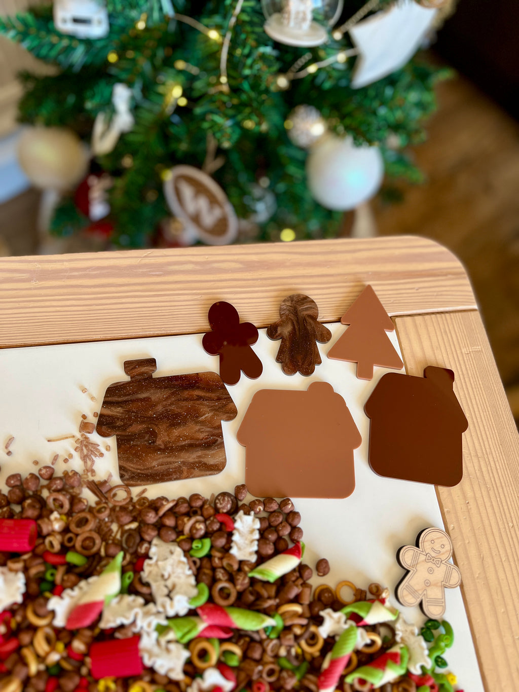 Marbled and solid brown house, tree, and gingerbread-shaped cutouts on wooden table with colorful sensory mix below
