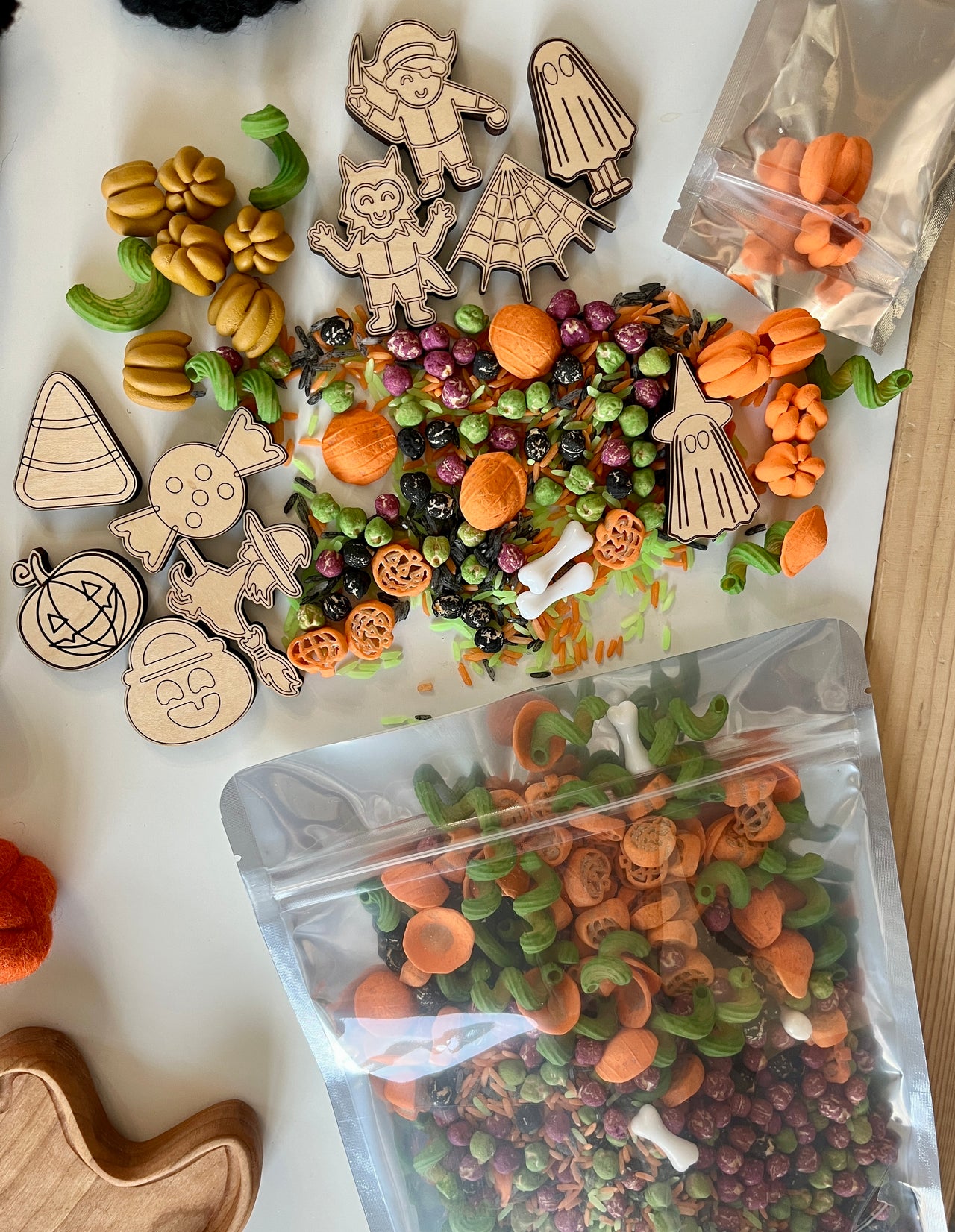 Halloween-themed sensory bin materials including wooden characters, pumpkin shapes, bones, and colorful dried pasta on a white surface