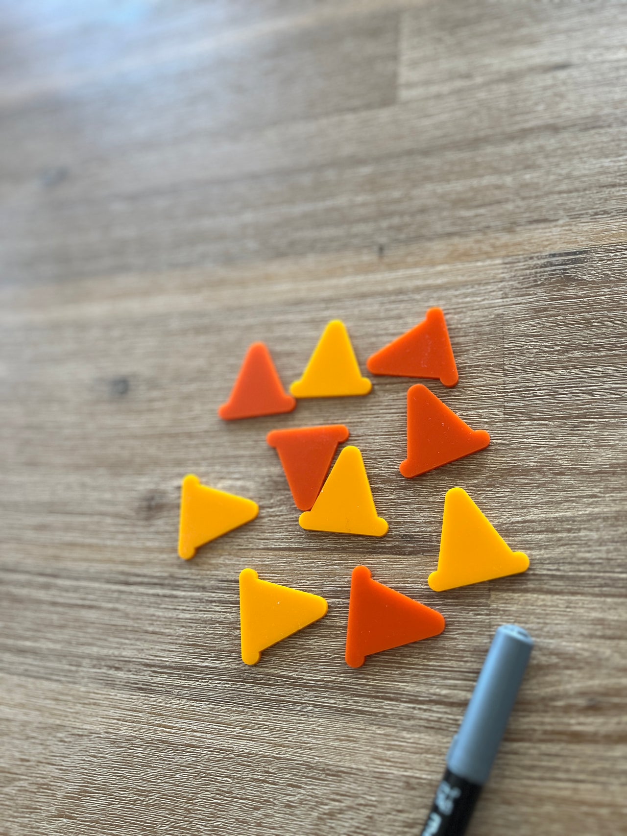Twelve small orange and yellow cone shapes arranged on a wooden surface alongside a gray marker, Little Dry Erasables - Construction Cones, handcrafted, homeschool, education resources.