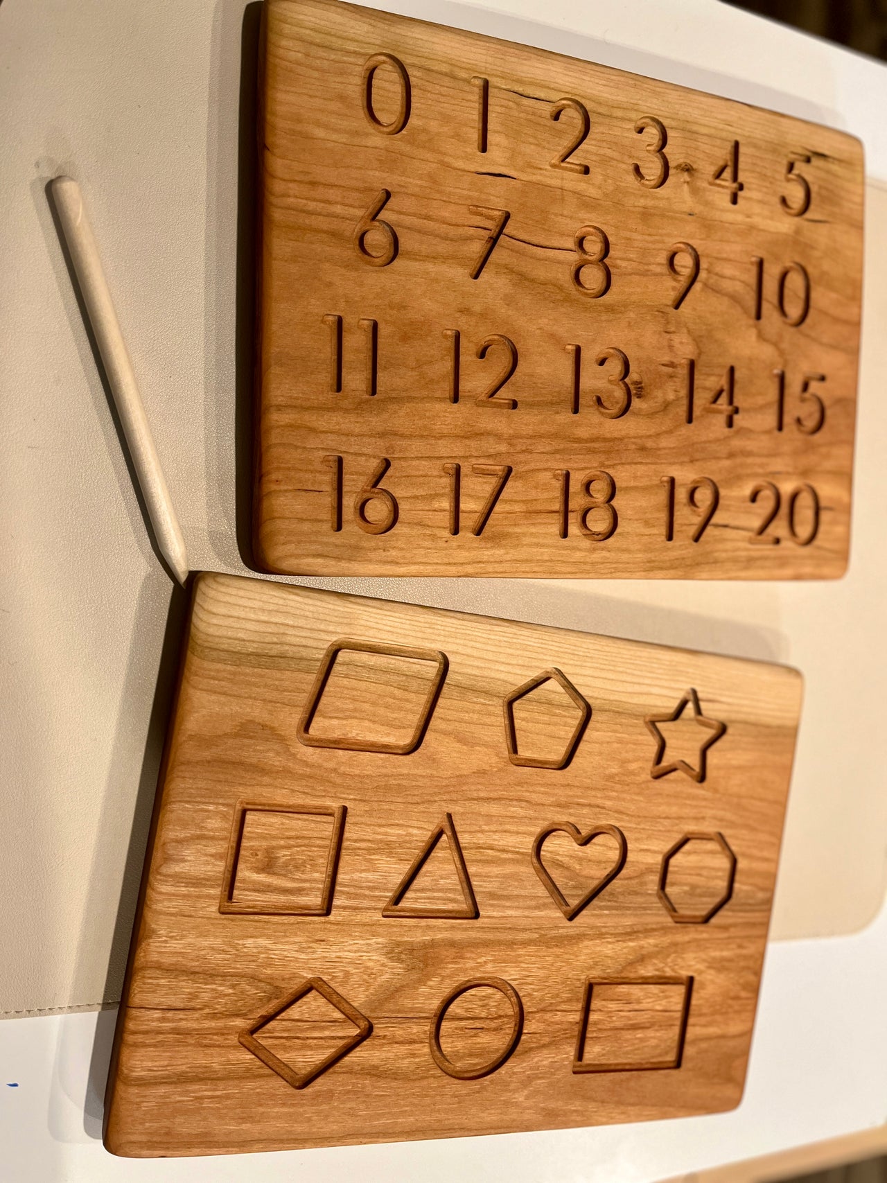 Wooden puzzle boards with engraved numbers and geometric shapes alongside a wooden stylus on a white surface