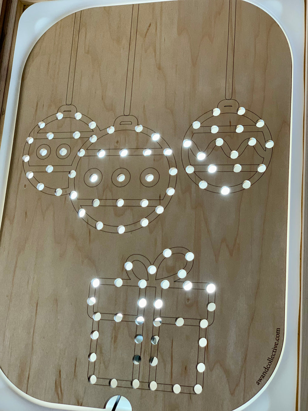 Wooden Flisat insert with light-up holes forming Christmas balls and gift shapes on light wood surface