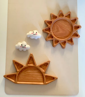 Two wooden sun-shaped trays on beige surface alongside two small smiling felt cloud decorations
