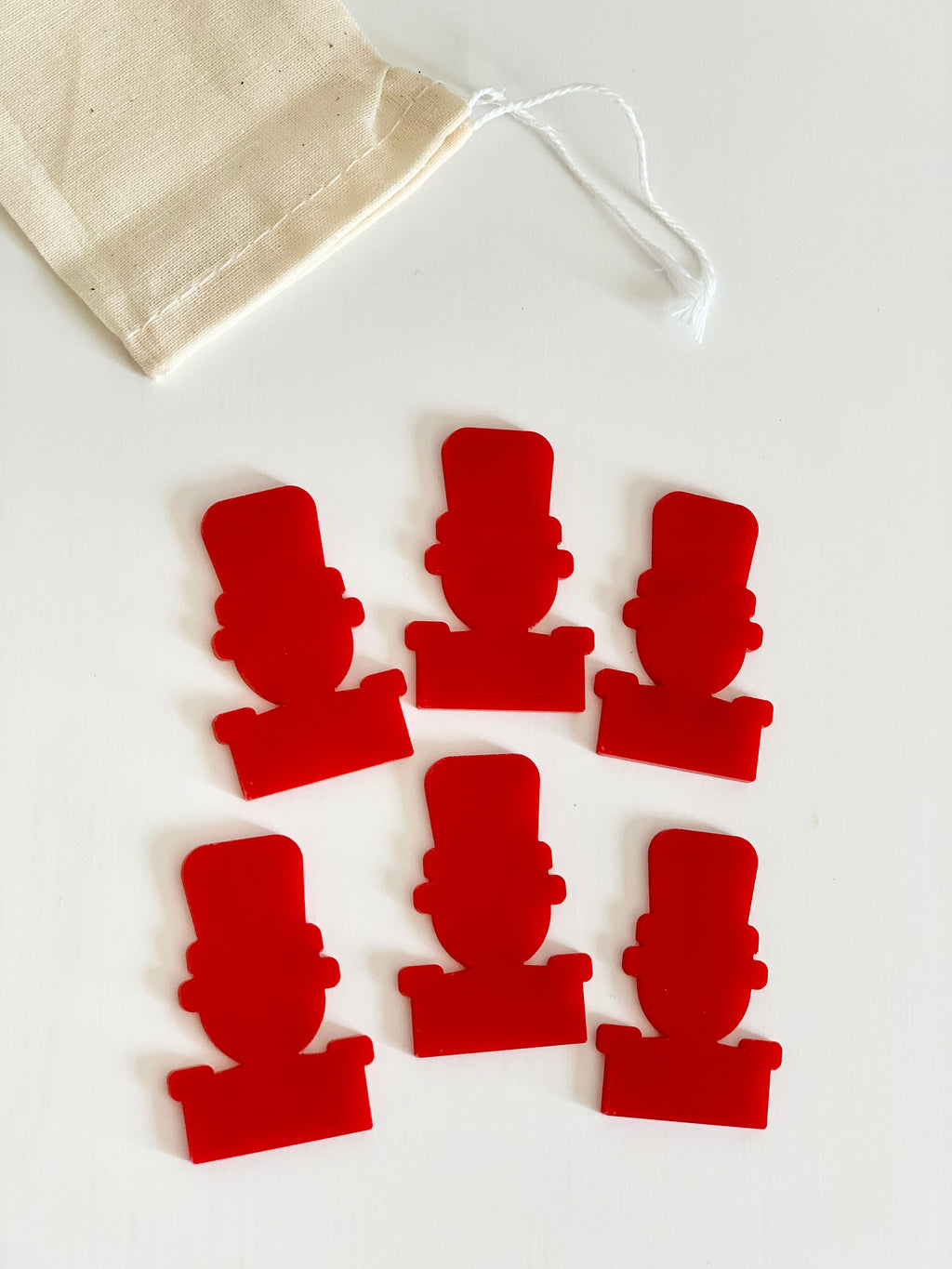 Set of six red nutcracker-shaped dry erasable pieces with a beige drawstring storage bag on white background
