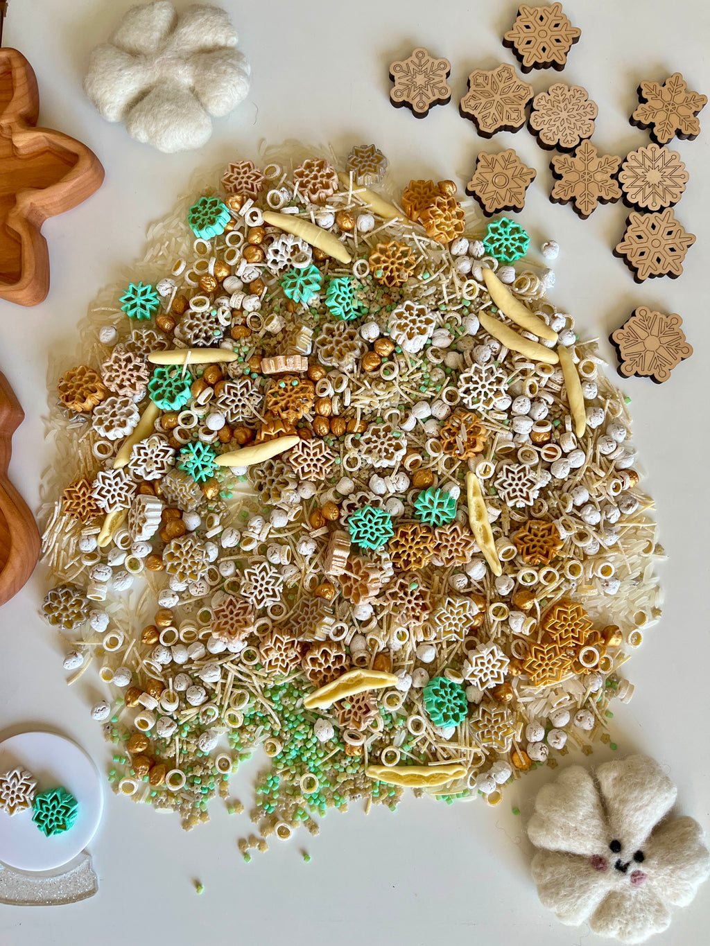 Scattered natural sensory materials with small wooden snowflake cutouts and felt flower shapes on white background
