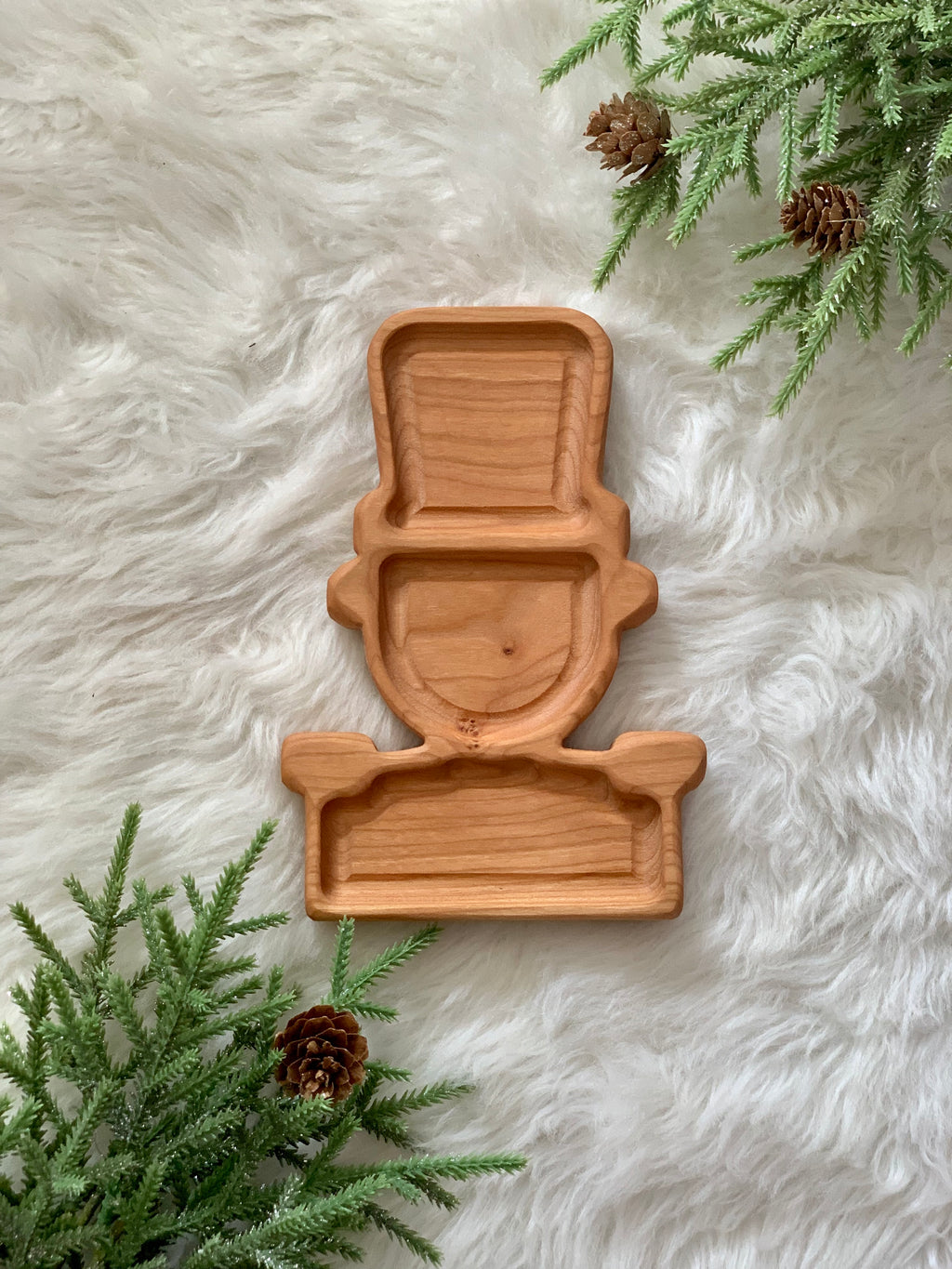 Wooden sensory tray shaped like a little soldier boy with sections on white fur background and pine branches